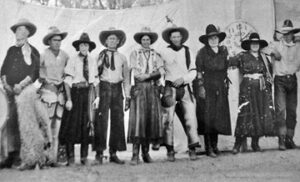 A group of cowboys and cowgirls in front of banner for the Bill Penney Wild West